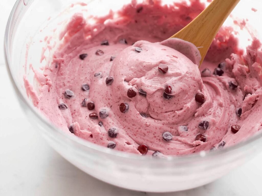 Slice of cherry chip cake with pink frosting, cherry on top, and white chocolate drizzle