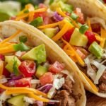 Ground beef tacos with seasoned meat, fresh shredded lettuce, ripe diced tomatoes, avocado slices, and shredded cheese served on a rustic wooden board with lime wedges, perfect for family dinners and zero waste meal ideas using rotisserie chicken.