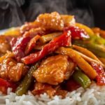 "Close-up of stir-fry with glossy sauce, golden chicken, and colorful veggies on a bed of steamed rice"