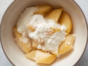 Zoomed-in view of potato wedges coated with white cornstarch in a mixing bowl, ready to fry.